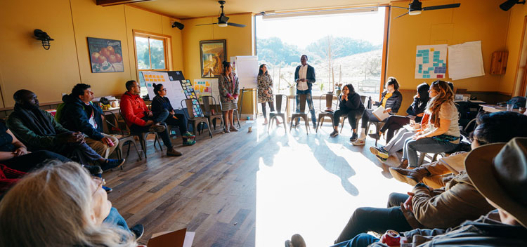 a group of retreat participants circle up to have a conversation on the ground floor of the Barn with sunlight pouring in through open doors
